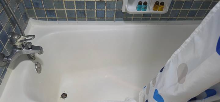 White bathtub with shower curtain and small toiletry bottles against mosaic tiles.