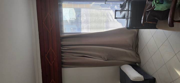 Hotel room corner with closed drapes, suitcase and part of a single bed.