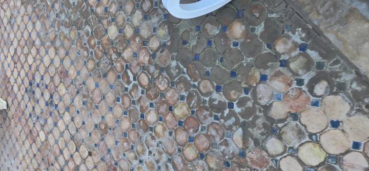 Detailed view of worn mosaic paving stones with part of a white plastic chair.