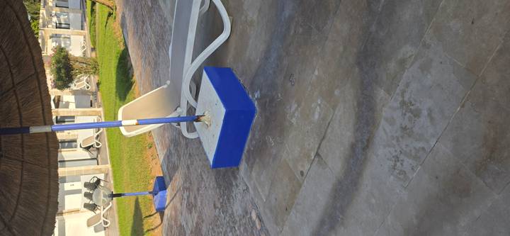 Poolside area with blue umbrella stand, white lounge chair and green lawn.