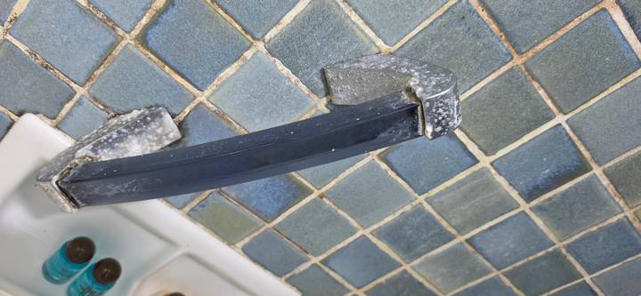 Close-up of a broken plastic grab bar on a tiled bathroom wall with toiletries nearby.