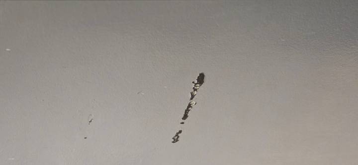 Close-up of a grey wall with a long scratch exposing underlying material.