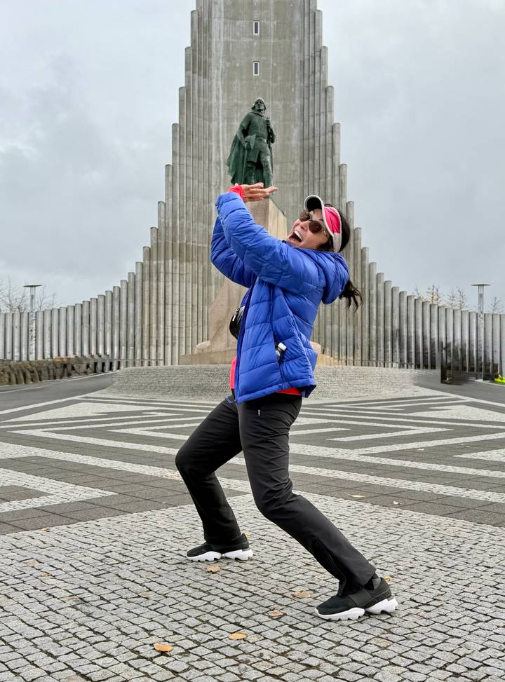 Energetic traveller pretends to hold up Hallgrimskirkja church while standing on patterned pavement.