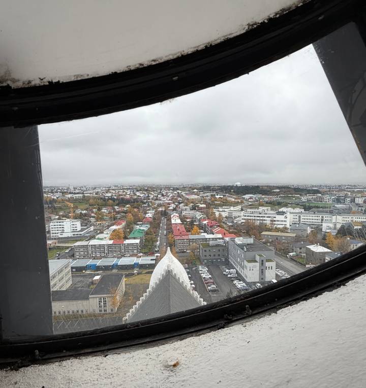 View through a window frame shows Reykjavik’s colourful rooftops spreading beneath a grey sky.