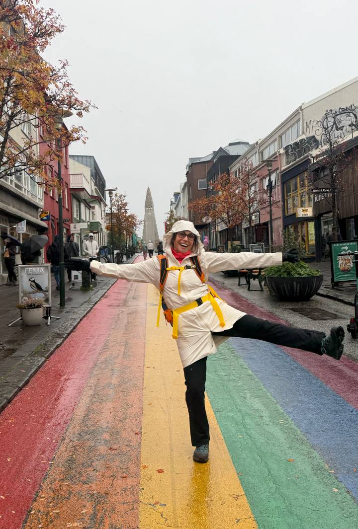 Traveller joyfully stretches across Reykjavik’s colourful rainbow street with Hallgrimskirkja visible far behind.