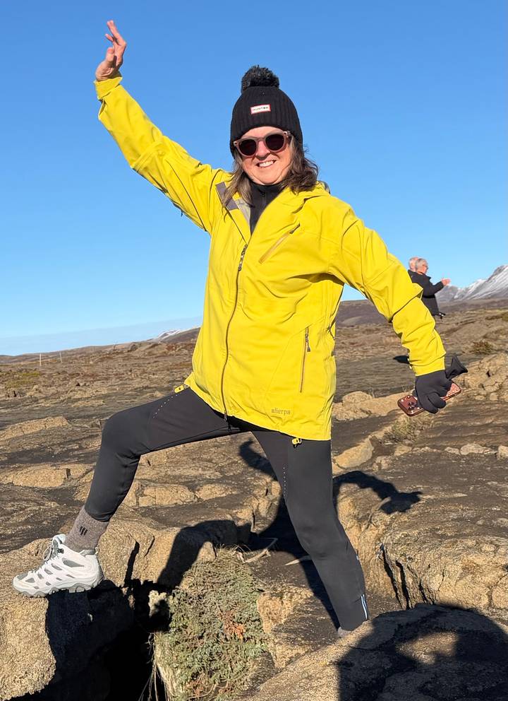 Traveller in yellow jacket strikes a triumphant pose on rocky lava fields under blue sky.