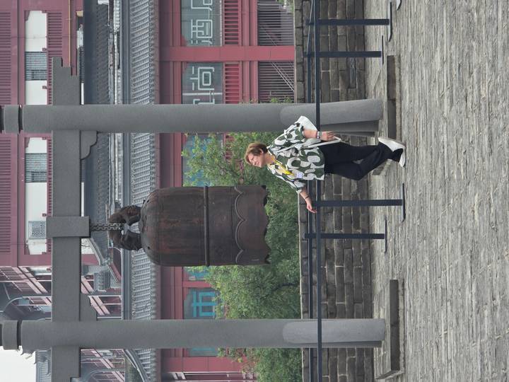 Visitor gazes up at a large bronze bell suspended on an ancient city wall platform in China.
