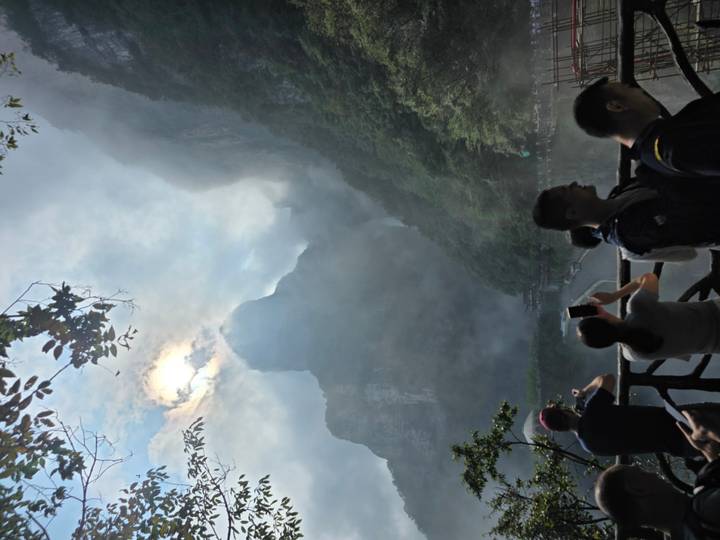 Tourists photograph mist-shrouded quartz sandstone peaks of Zhangjiajie rising dramatically into the clouds.