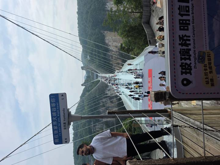 Crowds walk across the glass-bottom Zhangjiajie Grand Canyon Bridge suspended high above a forested gorge.