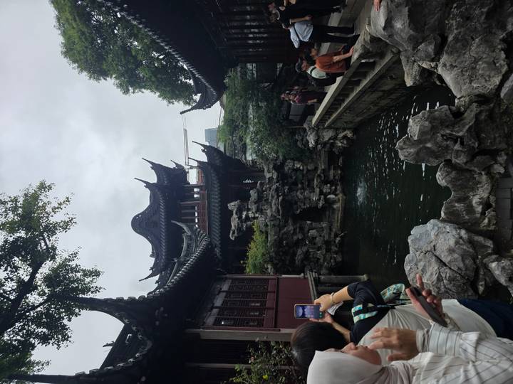 Traditional pavilion and rock garden of Yu Garden in Shanghai with visitors taking photos beside a koi pond.