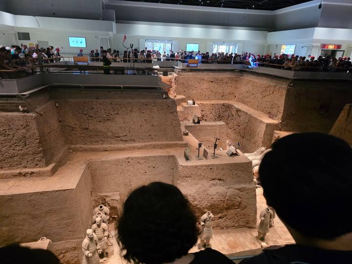 Overlook into a busy archaeological pit where Terracotta Warriors are being excavated while tourists observe from above.
