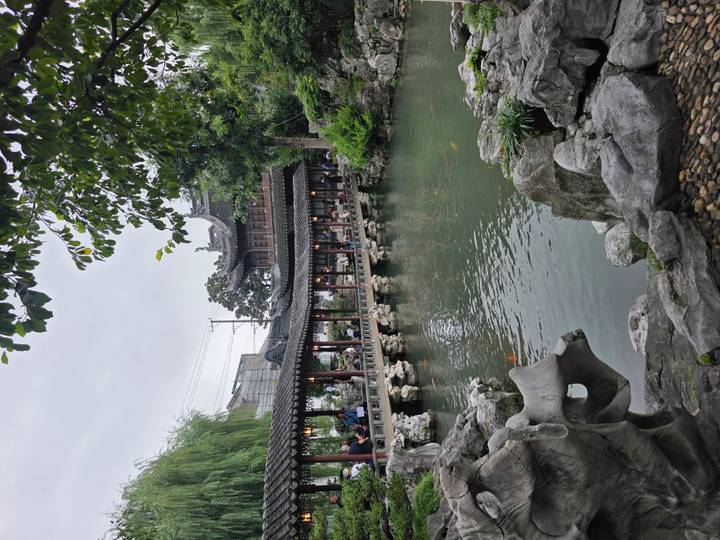 Elegant covered walkway lined with red columns crosses a tranquil pond with koi fish in Yu Garden.