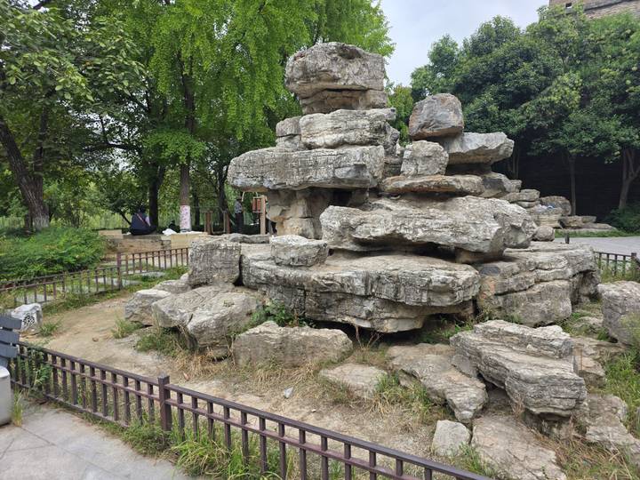 Cluster of weathered limestone rocks arranged in a public park area with sparse grass and trees.
