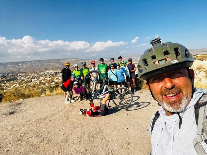 Cheerful group of mountain bikers posing on a dusty track overlooking Cappadocia’s rugged valleys under a bright sky.
