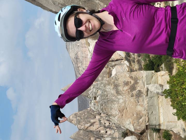 Cyclist in bright pink top poses playfully in front of Cappadocia’s fairy-chimney backdrop, arm extended as if pinching a distant rock.