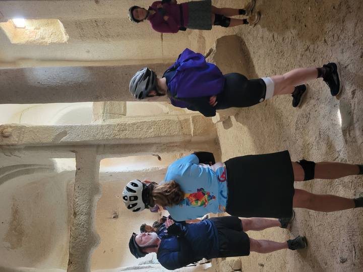Helmeted cyclists explore the cool interior of a rock-cut church with high columns and soft light.