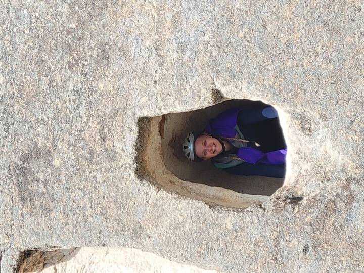 Cyclist peeks and smiles from a small cave window carved into tan rock.