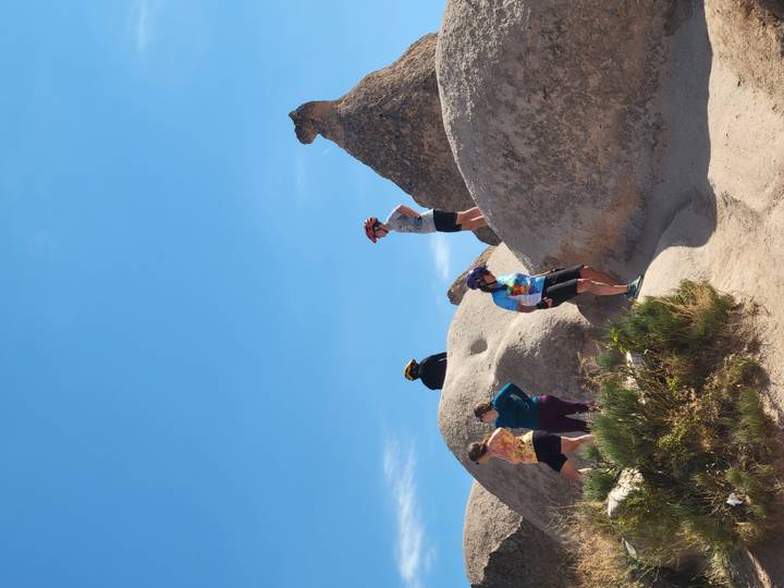 Group of cyclists stand atop smooth beige rock mounds against Cappadocia’s deep blue sky.