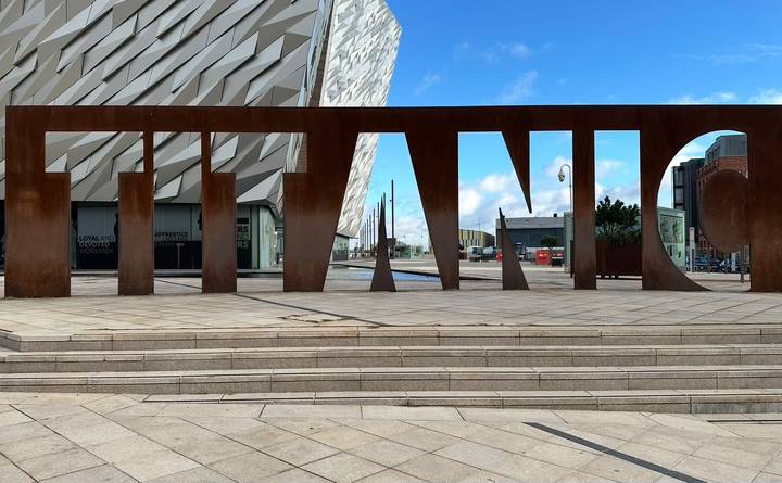 The bold steel letters spelling TITANIC stand before the contemporary facade of Titanic Belfast museum.
