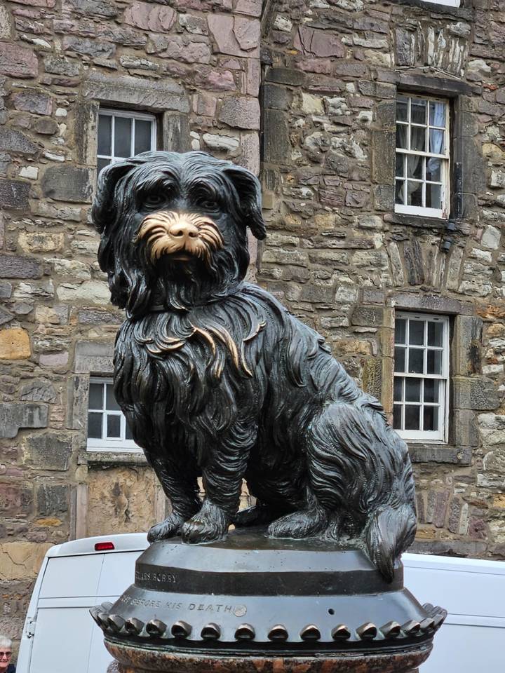 The bronze statue of Greyfriars Bobby stands against a backdrop of old stone buildings.
