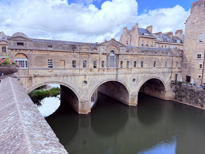Historic stone bridge lined with Georgian buildings spanning a calm river in a classic English city.