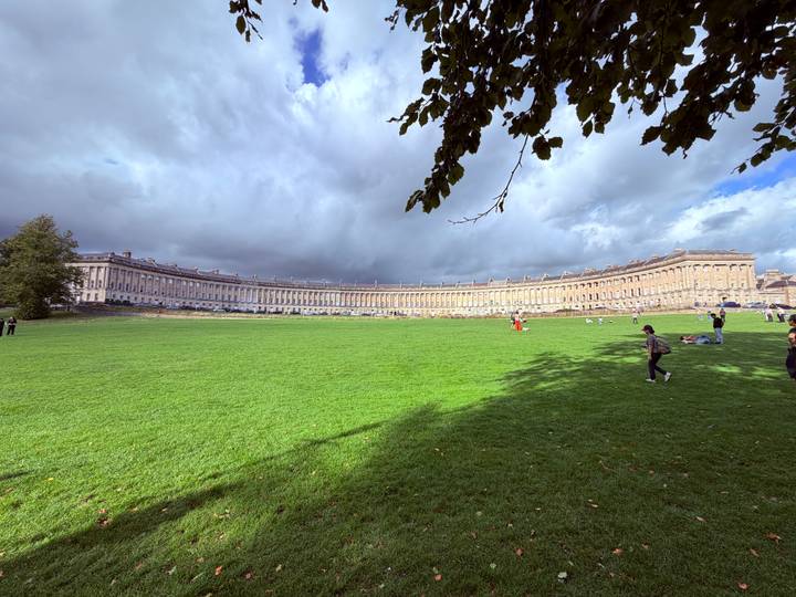 Sweeping crescent of Georgian terrace houses framing a vast green lawn under dramatic clouds.