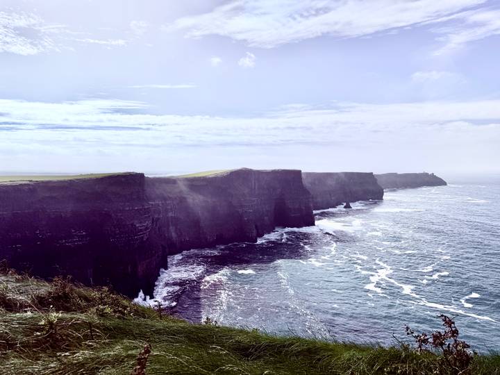 Dramatic sea cliffs plunging into a churning Atlantic Ocean with mist drifting across the rugged coastline.