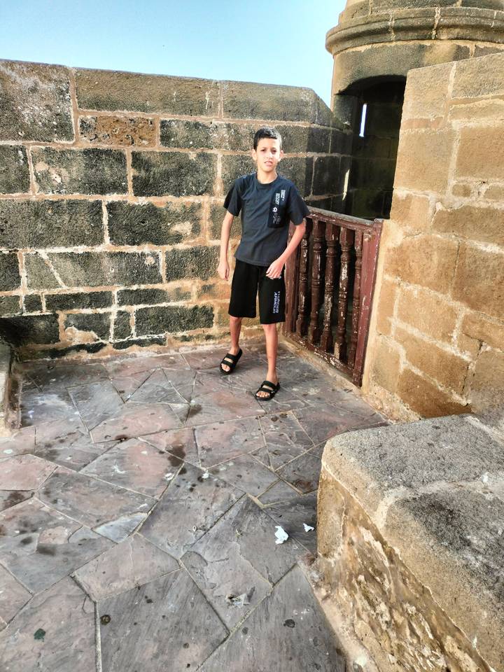 Cropped image of a boy’s lower body standing in a weathered stone nook, offering minimal context.