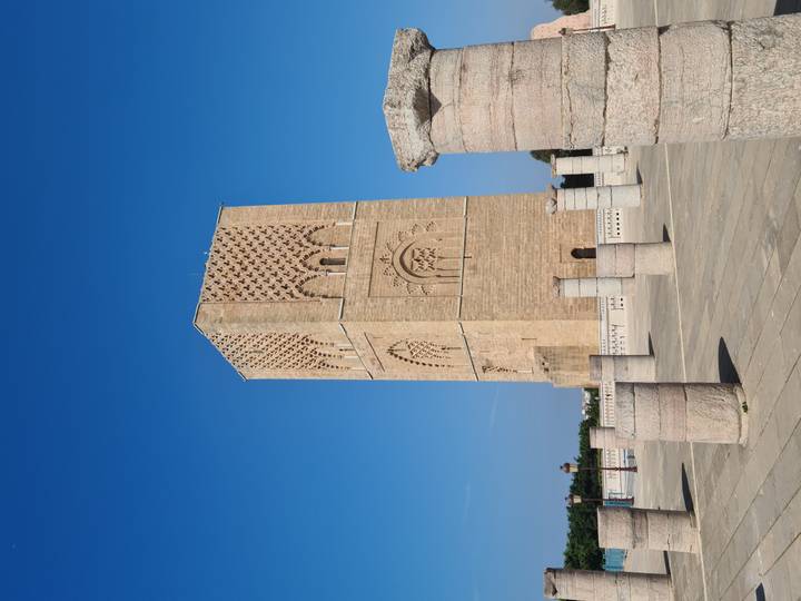 The sandstone Hassan Tower rises under a vivid blue sky, surrounded by rows of unfinished columns.