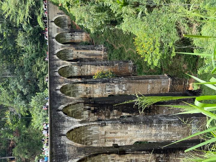 Crowds walk across Sri Lanka’s iconic Nine-Arch Bridge as a lush jungle valley drops below the tall stone arches.