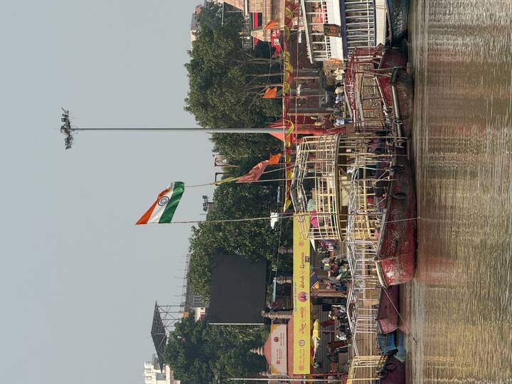 Wooden boats moor along the Ganges River ghats beneath a large Indian flag fluttering in Varanasi.