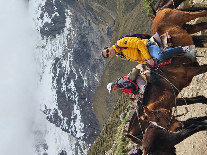Two trekkers on horseback pause before snow-covered Andean mountains shrouded in mist.