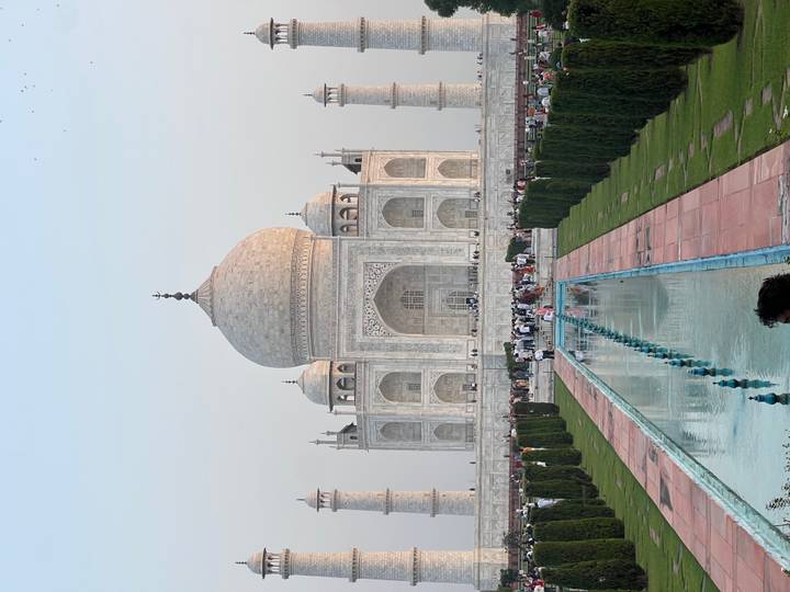 Iconic frontal view of the Taj Mahal with reflecting pool and crowds of visitors in the gardens at dusk.