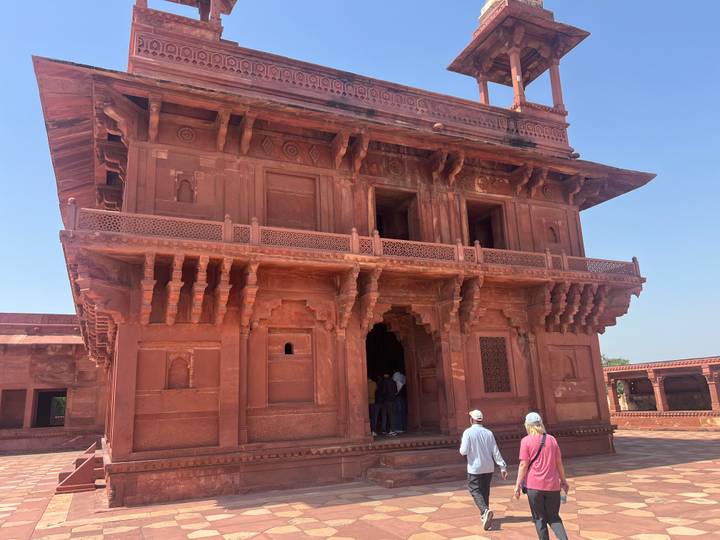 Red sandstone palace building in Fatehpur Sikri with a small group of tourists approaching the entrance.