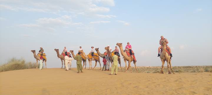 Travellers ride colourfully saddled camels led across golden desert dunes.