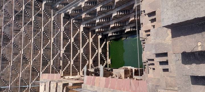 Geometric terraced steps of Chand Baori stepwell descend to green water.