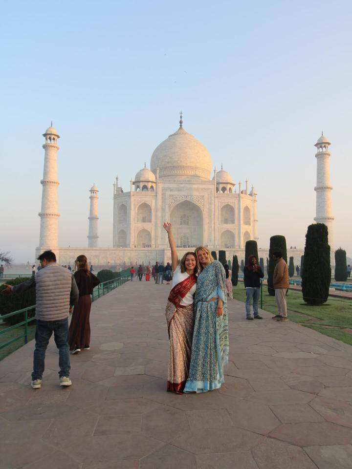 Two women in saris celebrating before Taj Mahal at early morning light