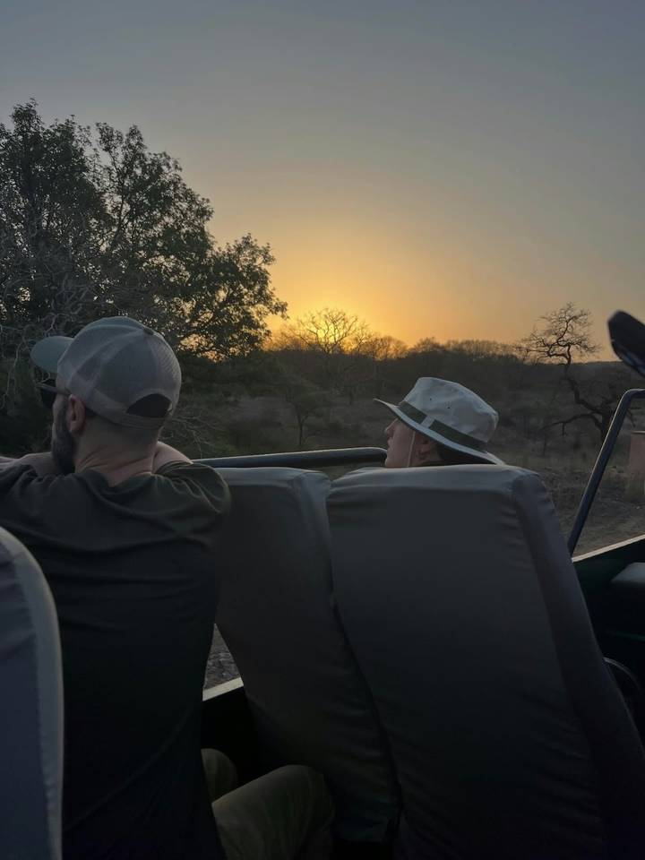 Travelers seated in open jeep watching sunset over dry forest landscape