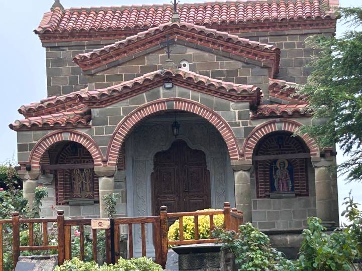 Small stone chapel with red-tiled arches and wooden door set against greenery.