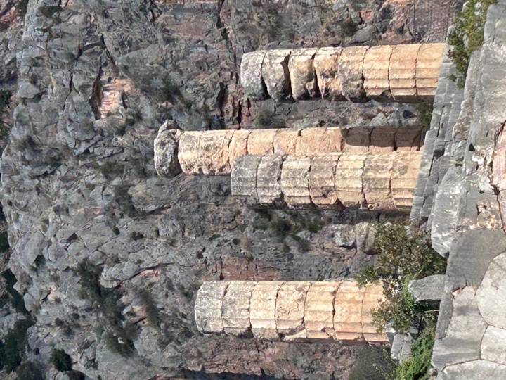 Weathered ancient stone columns standing before a rugged mountain cliff.