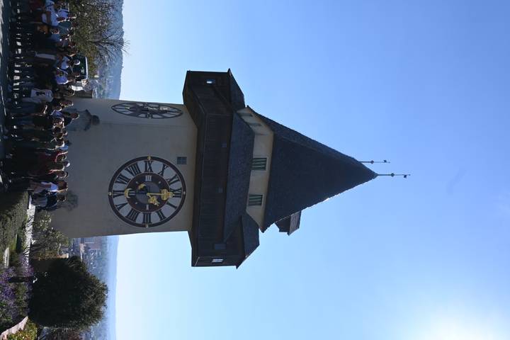 Historic Uhrturm clock tower on hilltop above Graz with large tour group gathered below.