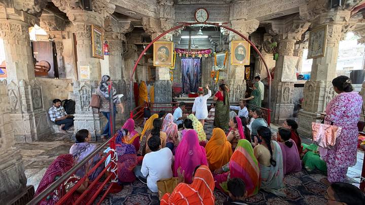 Colorful gathering of worshippers sitting inside an ornately carved temple during a religious ceremony.