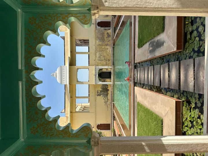 Two swimmers enjoy a turquoise palace pool framed by ornate arches and lily pads.