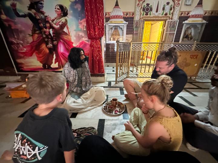 Family sits with a guru inside a dimly lit temple chamber during a blessing ceremony.
