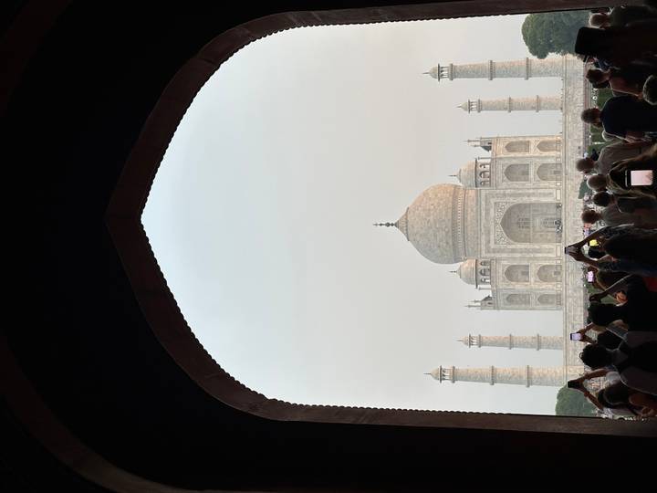 Iconic Taj Mahal framed by a dark arch with a crowd of visitors taking photos in the foreground.