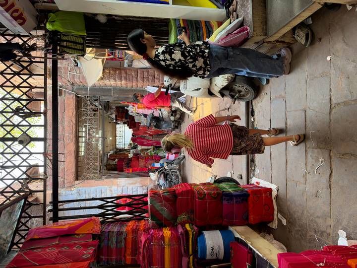 Child walks into a bustling Indian textile market filled with colorful fabrics and scooters.