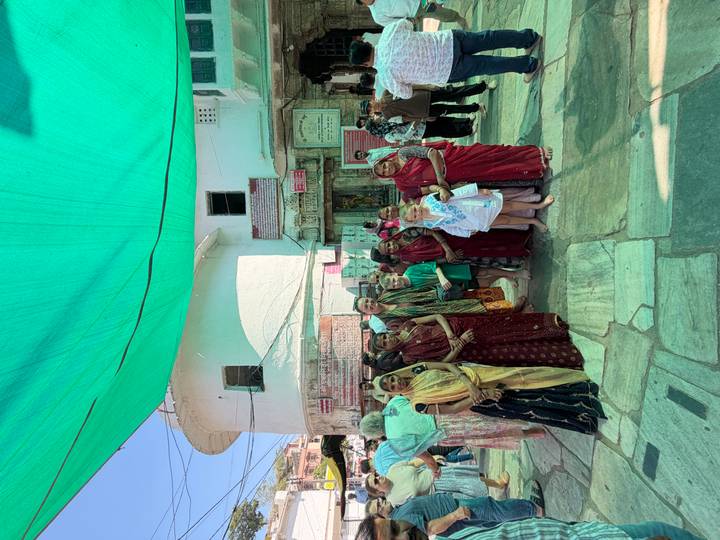 Tourist family and local women dressed in saris pose together under a green canopy in a temple courtyard.