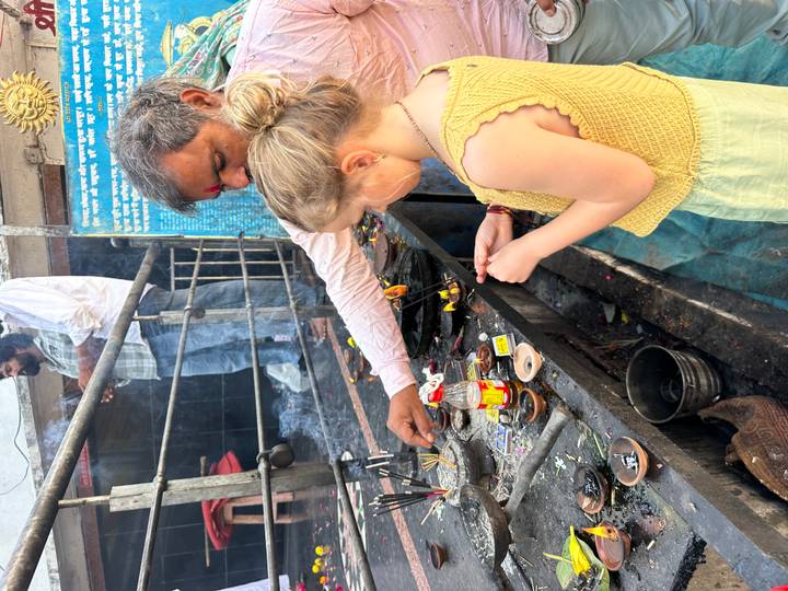 A girl and a man light incense offerings at a busy shrine filled with small oil lamps and smoke.