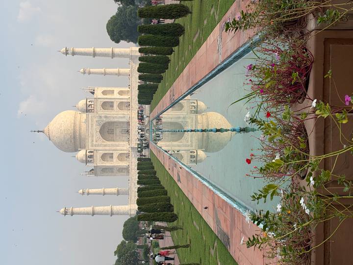 Centered view of the Taj Mahal perfectly reflected in the long pool framed by gardens and flowers.