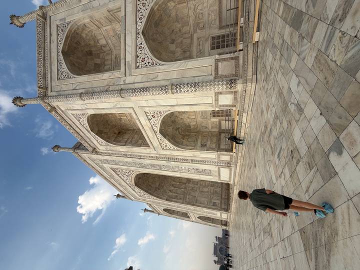 A boy walks along the ornate marble arches of the Taj Mahal, emphasizing intricate patterns.